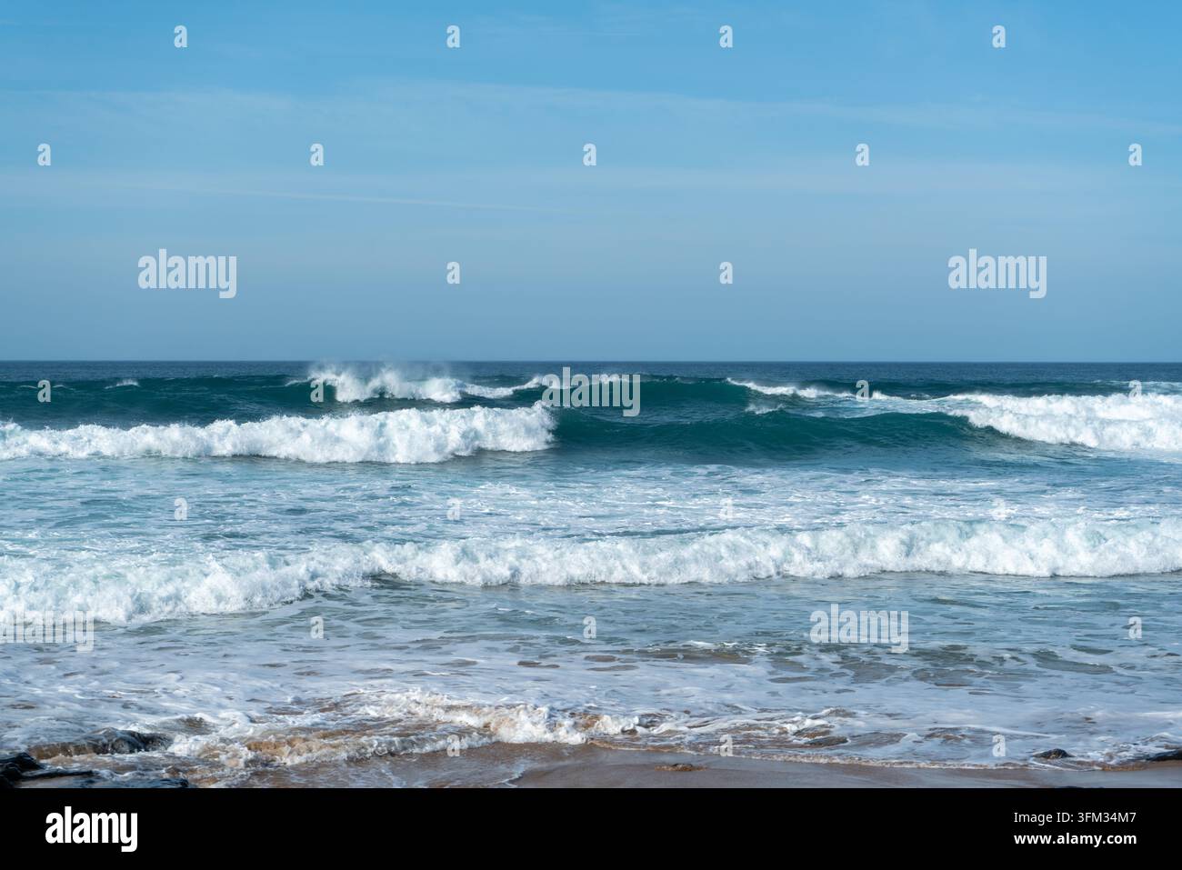 Questa splendida fotografia cattura potenti onde oceaniche che si infrangono su una spiaggia sabbiosa sotto un cielo limpido e luminoso. Il movimento dinamico dell'acqua crea Foto Stock