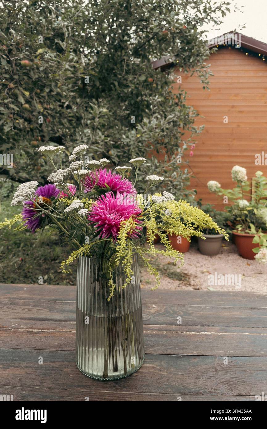 Bouquet autunnale di astri rosa e solidago in vaso di vetro su tavolo di legno - Immagine stock catturata con smartphone