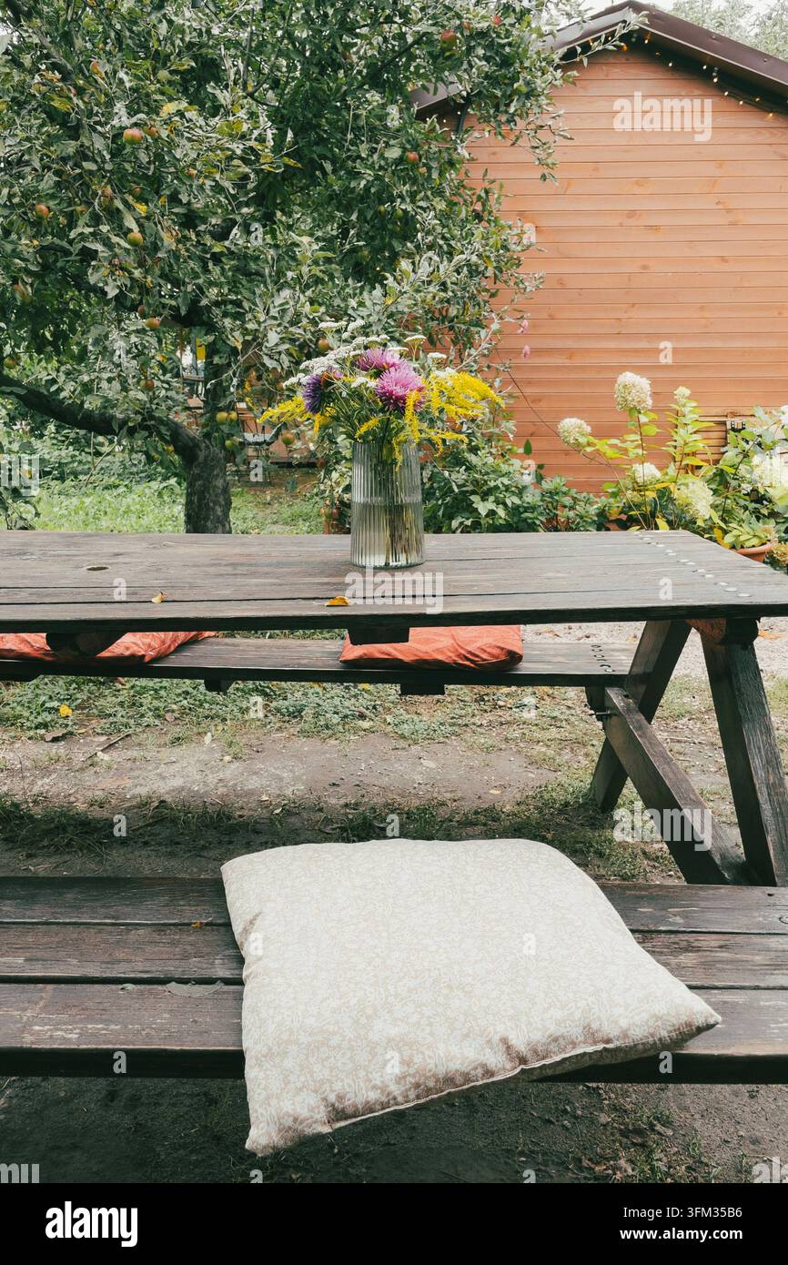 Mazzo di fiori selvatici in vaso di vetro su tavolo da picnic in legno nel giardino - Immagine stock catturata con smartphone