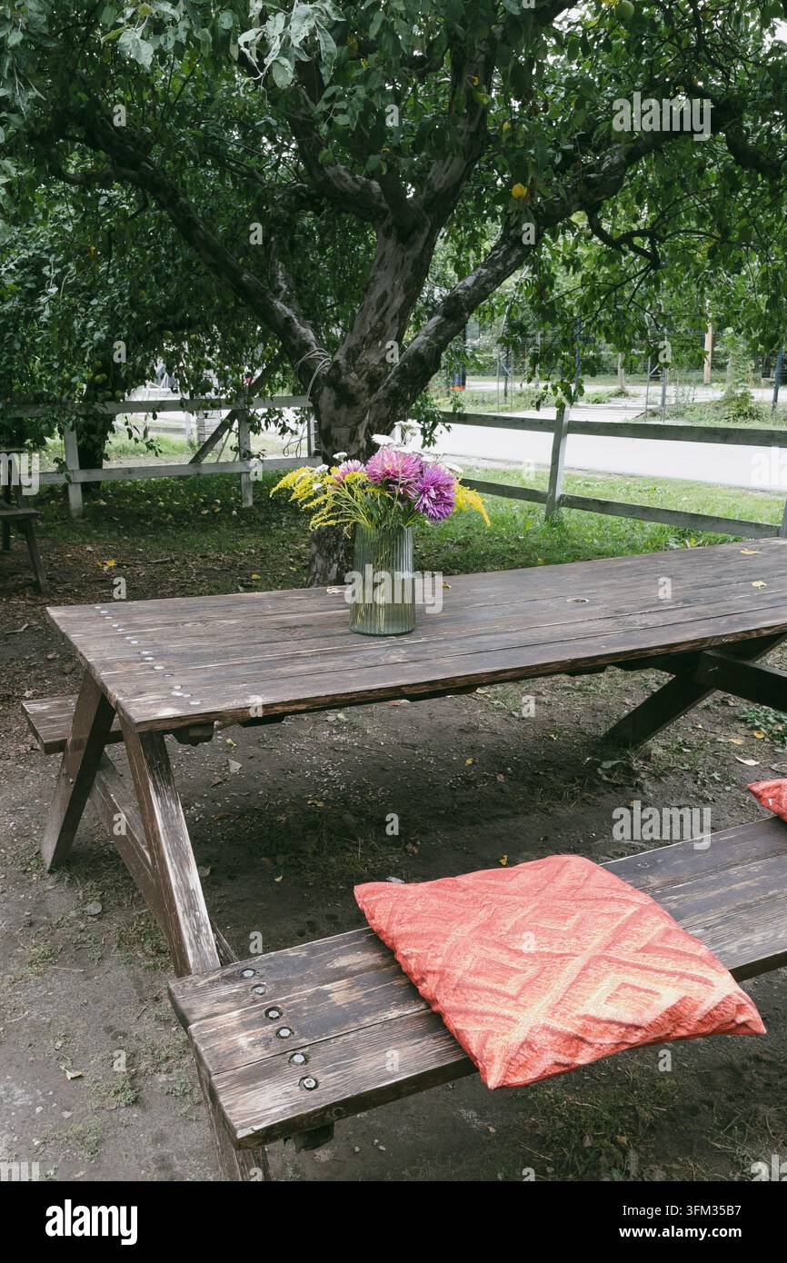 Mazzo di fiori selvatici in vaso di vetro su tavolo da picnic in legno in giardino - Immagine stock catturata con smartphone