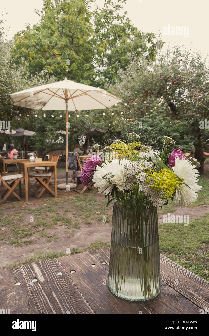 Mazzo di fiori selvatici in vaso di vetro su tavolo di legno in un caffè all'aperto - Immagine stock catturata con smartphone