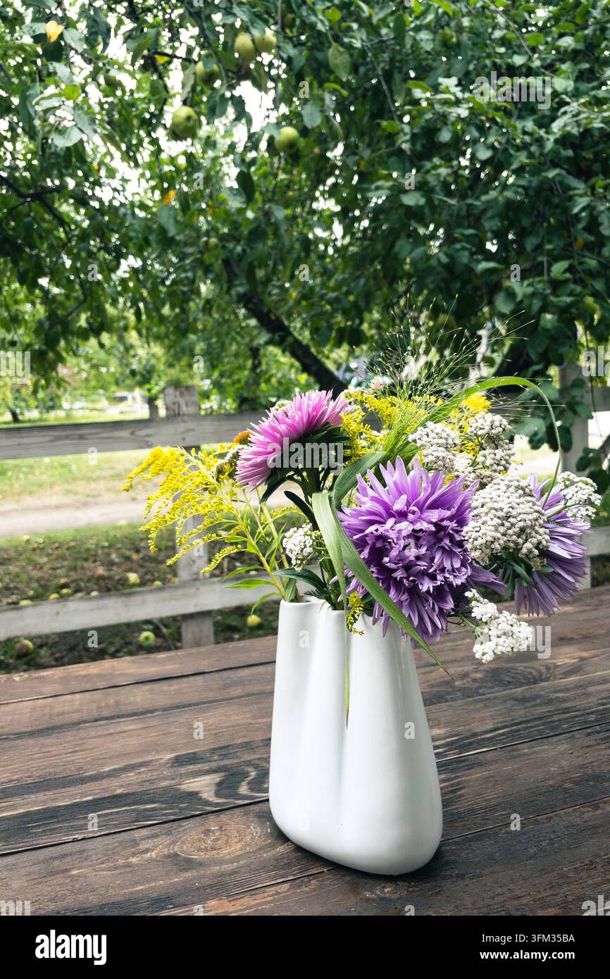 Mazzo di fiori selvatici con astri viola in vaso di ceramica su tavolo di legno - Immagine stock catturata con smartphone