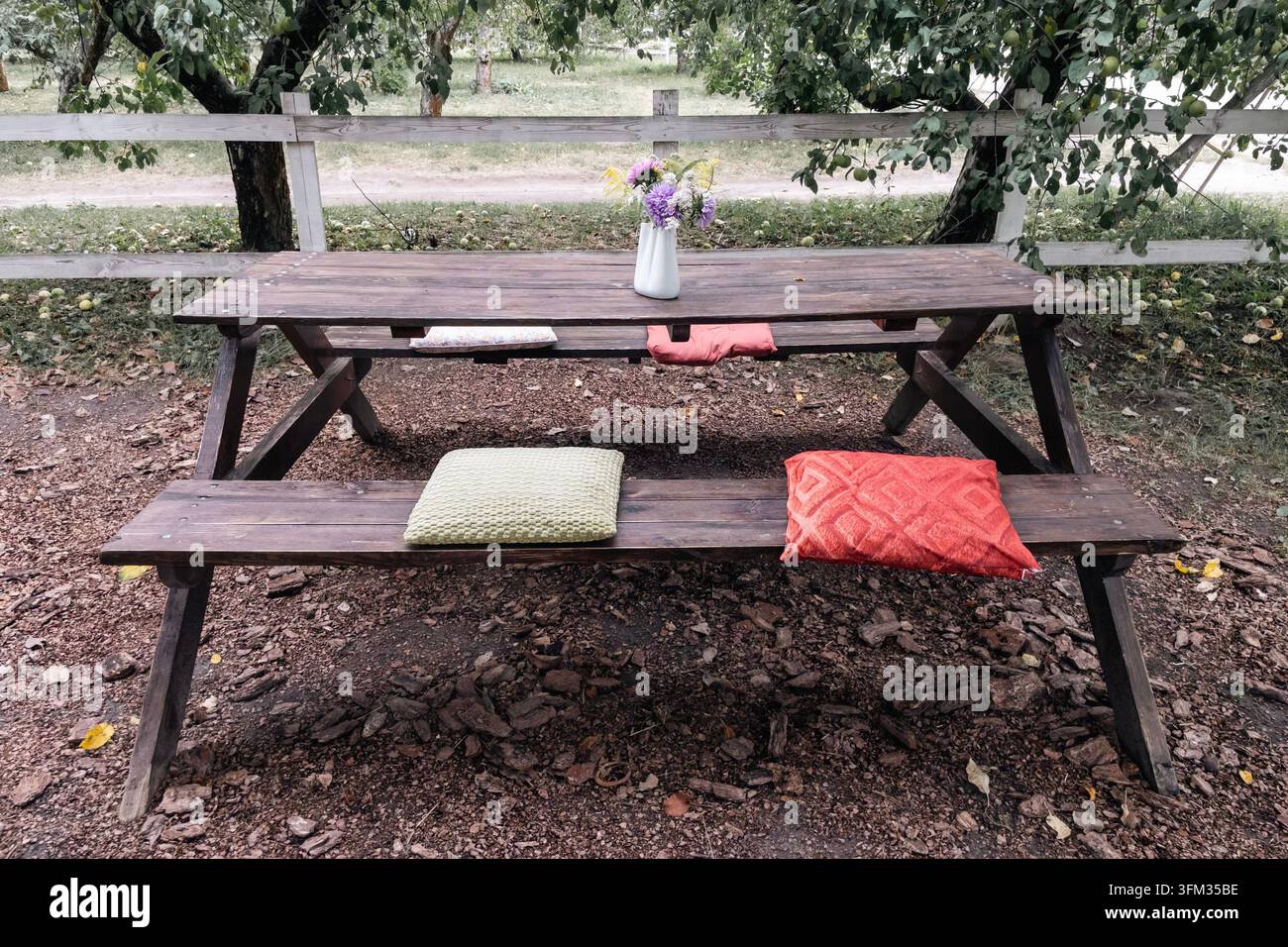 Tavolo da picnic in legno con cuscini e vaso di fiori selvatici in giardino - Immagine stock catturata con smartphone