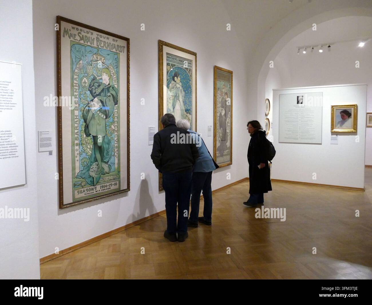 PRAGA - 17 nov. 2025 - Persone che interagiscono con opere d'arte dell'era Art Nouveau durante una mostra, apprezzando i design iconici dei poster di Mucha in un ambiente museale Foto Stock