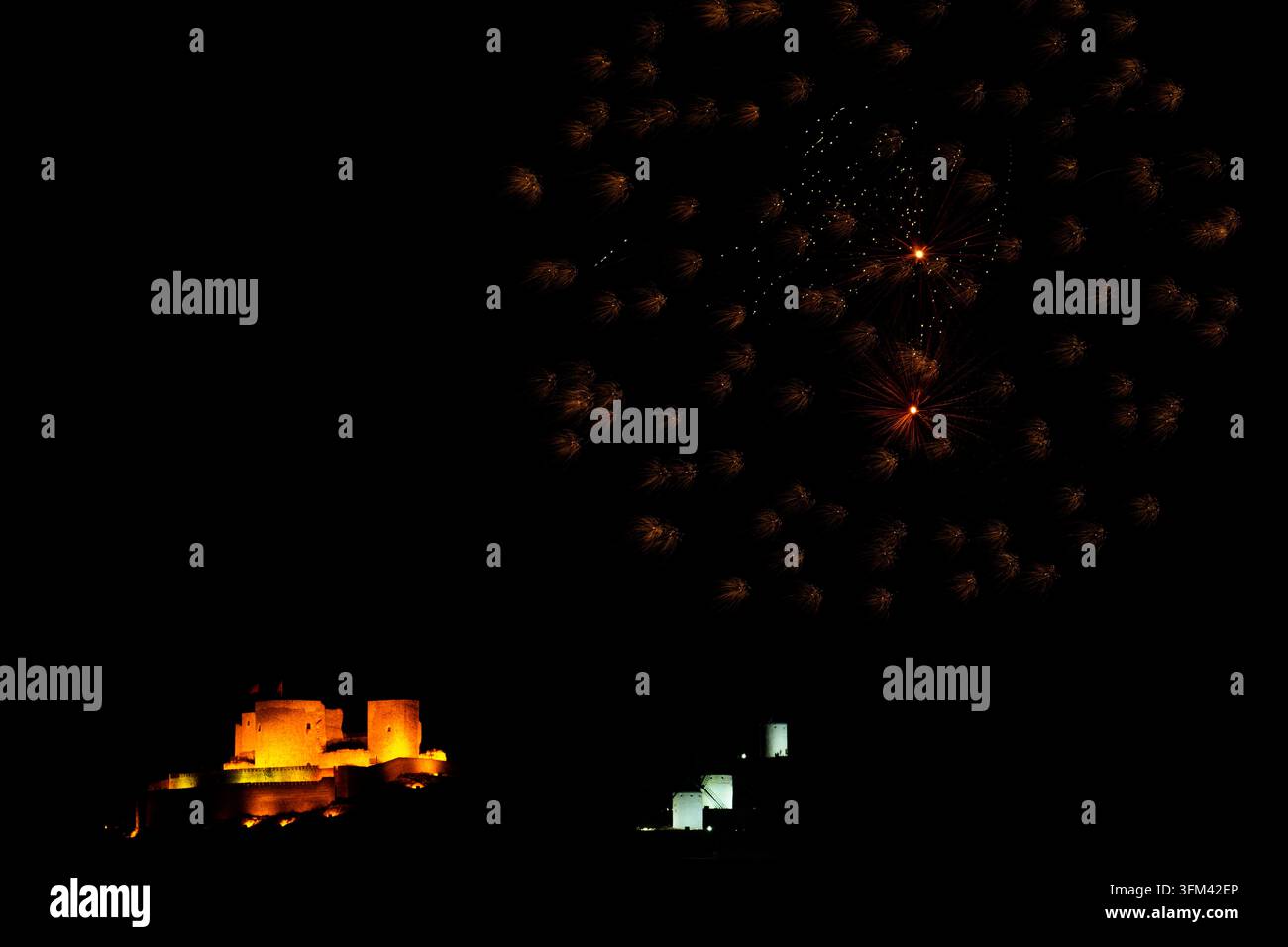 Il cielo notturno esplode con scintille d'fuochi d'artificio dorati. Un antico castello risplende calorosamente sotto. Una celebrazione silenziosa illumina l'orizzonte scuro. L'atmosfera del festival si fa sentire Foto Stock