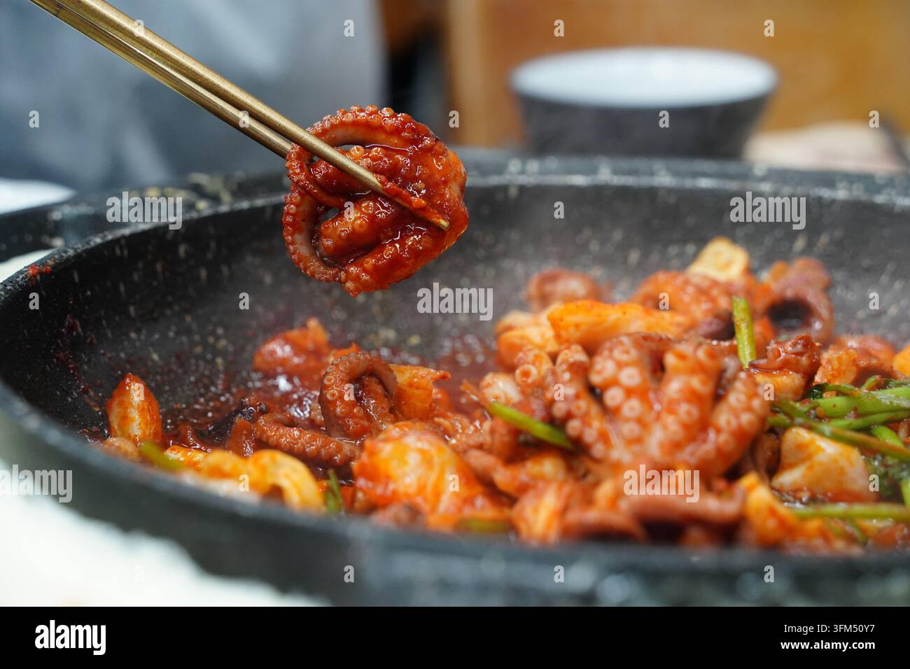 Prendere con le bacchette un polpo dalle zampe spinose fritto e piccante, autentico piatto coreano di frutti di mare (Jjukkumi-bokkeum) Foto Stock