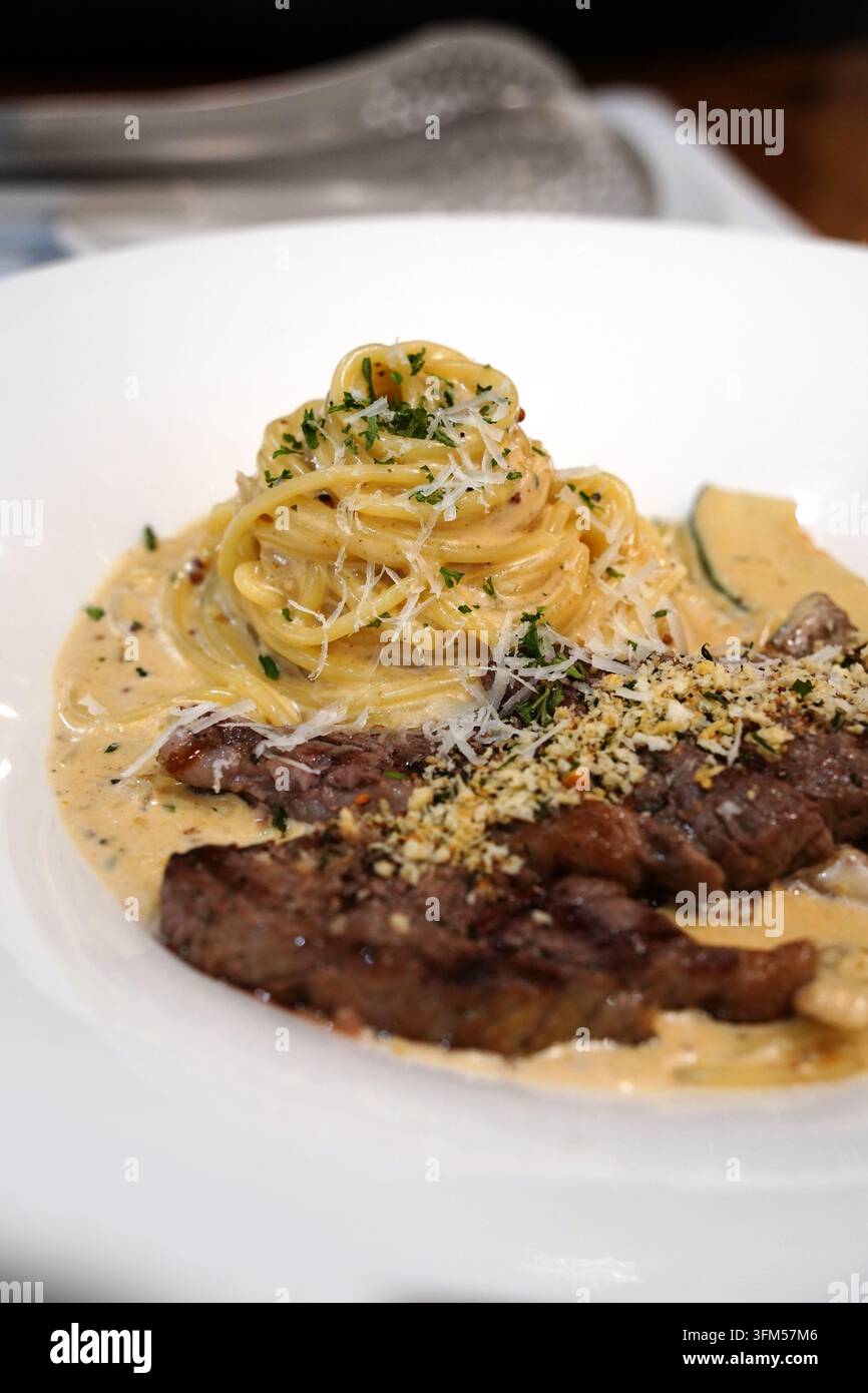 Pasta cremosa ricoperta da una fetta di bistecca di manzo tenera grigliata su un piatto bianco Foto Stock
