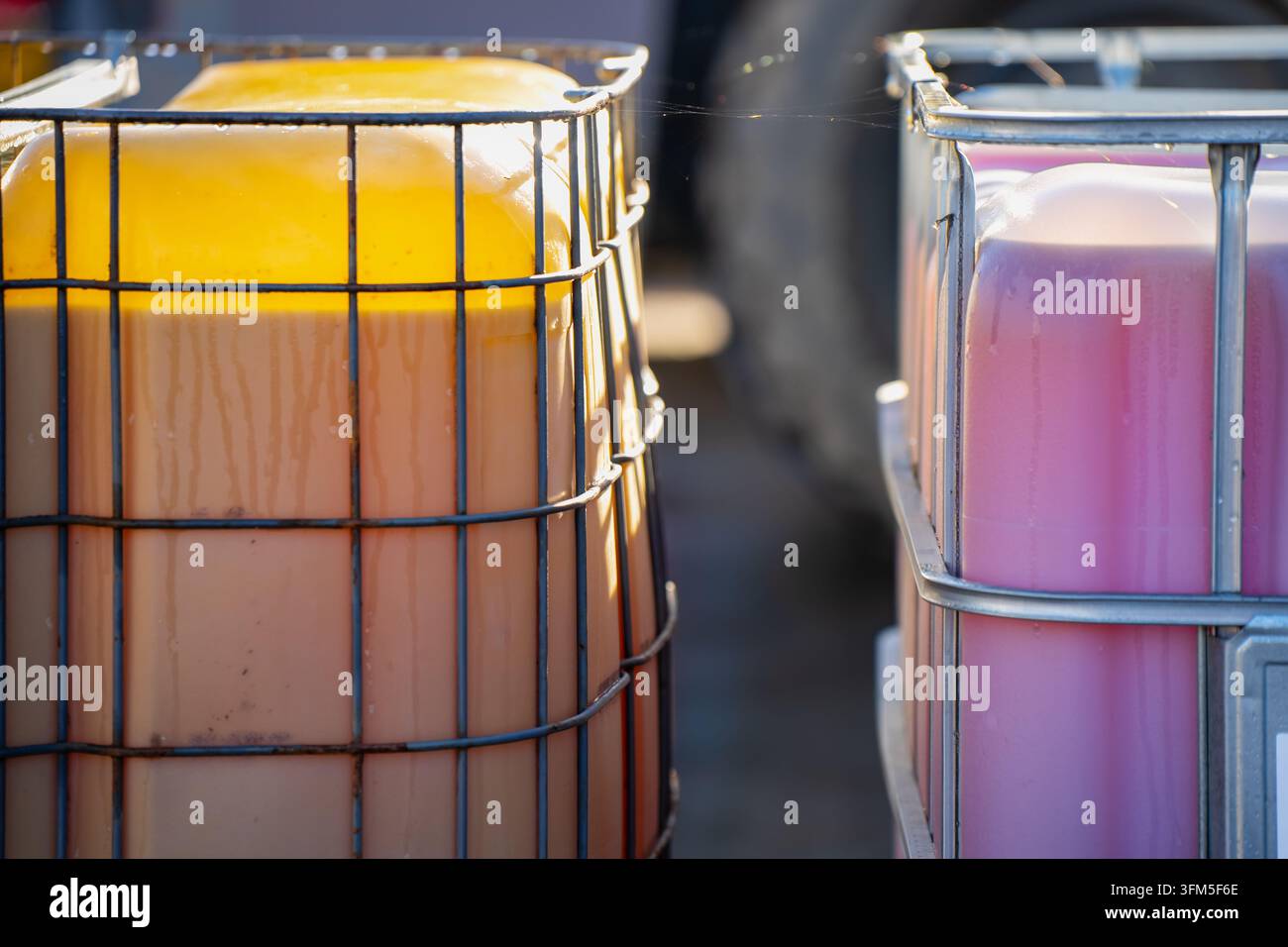 Due contenitori di liquido sfuso traslucidi si trovano all'interno di gabbie metalliche con livelli di riempimento visibili, mostrando imballaggi riutilizzabili per il deposito industriale di liquidi Foto Stock