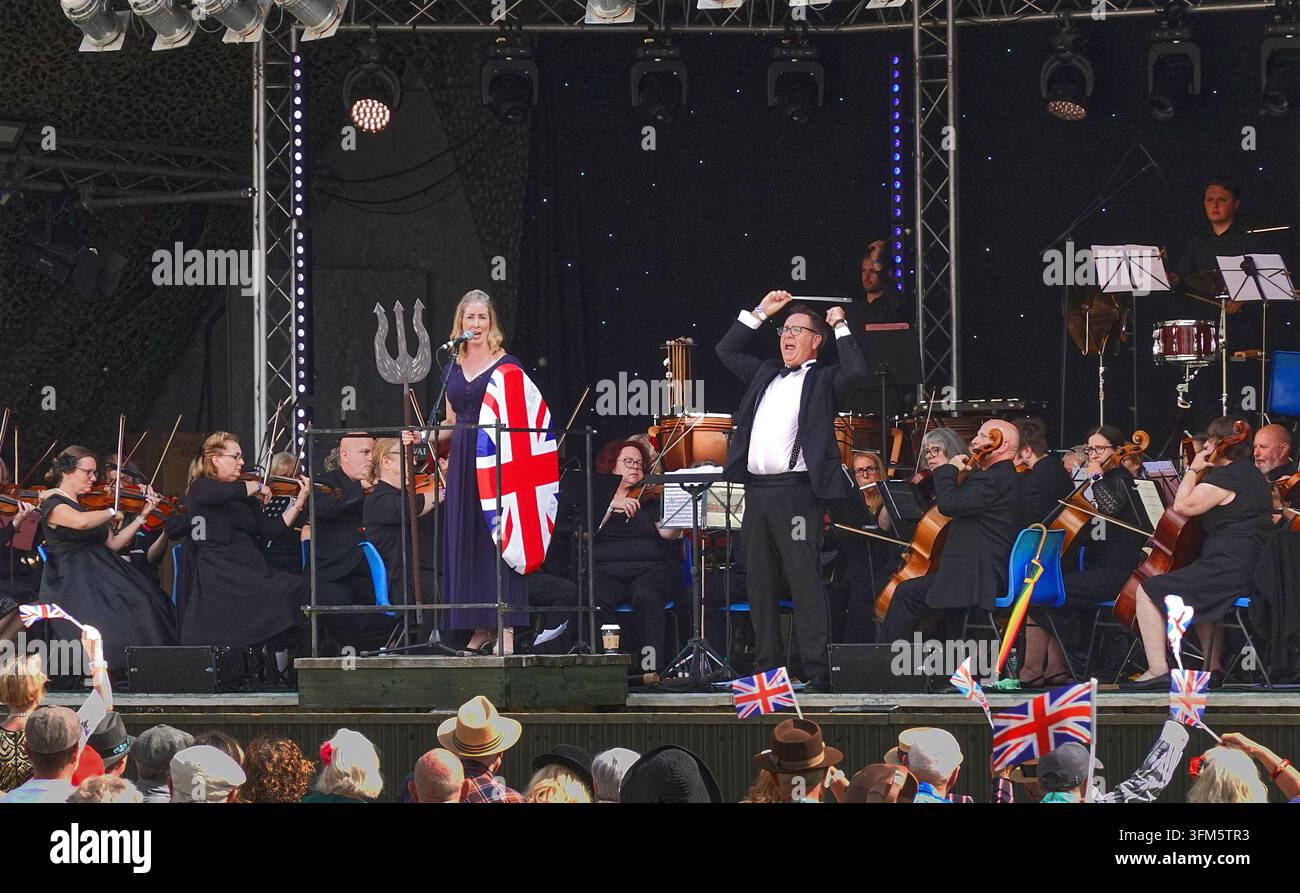 Cantante nei panni di Britannia e direttore d'orchestra che agita la bacchetta durante un concerto dei Proms – musica classica patriottica al festival musicale di Twinwood nel Bedfordshire, Inghilterra Foto Stock