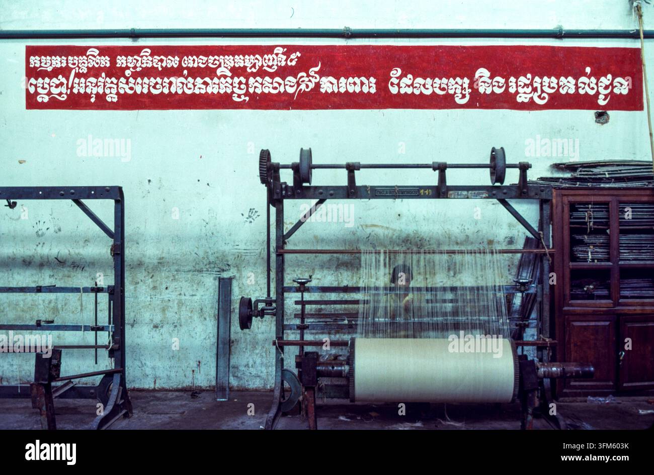 Lo slogan di questa fabbrica a Phnom Penh recita: "I lavoratori e il personale della Fabbrica di Tessitura n. 5 si impegnano a portare a termine tutti i compiti di produzione affidati loro dal Partito e dallo Stato." Foto Stock
