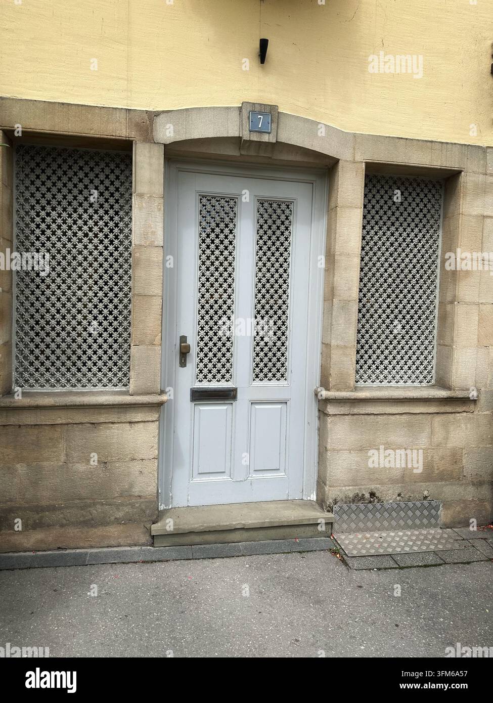 Facciata storica di un edificio con porta bianca e griglie decorative in ferro. Vista esterna dell'ingresso di un vecchio edificio in pietra con una porta in legno pallido, ornato Foto Stock