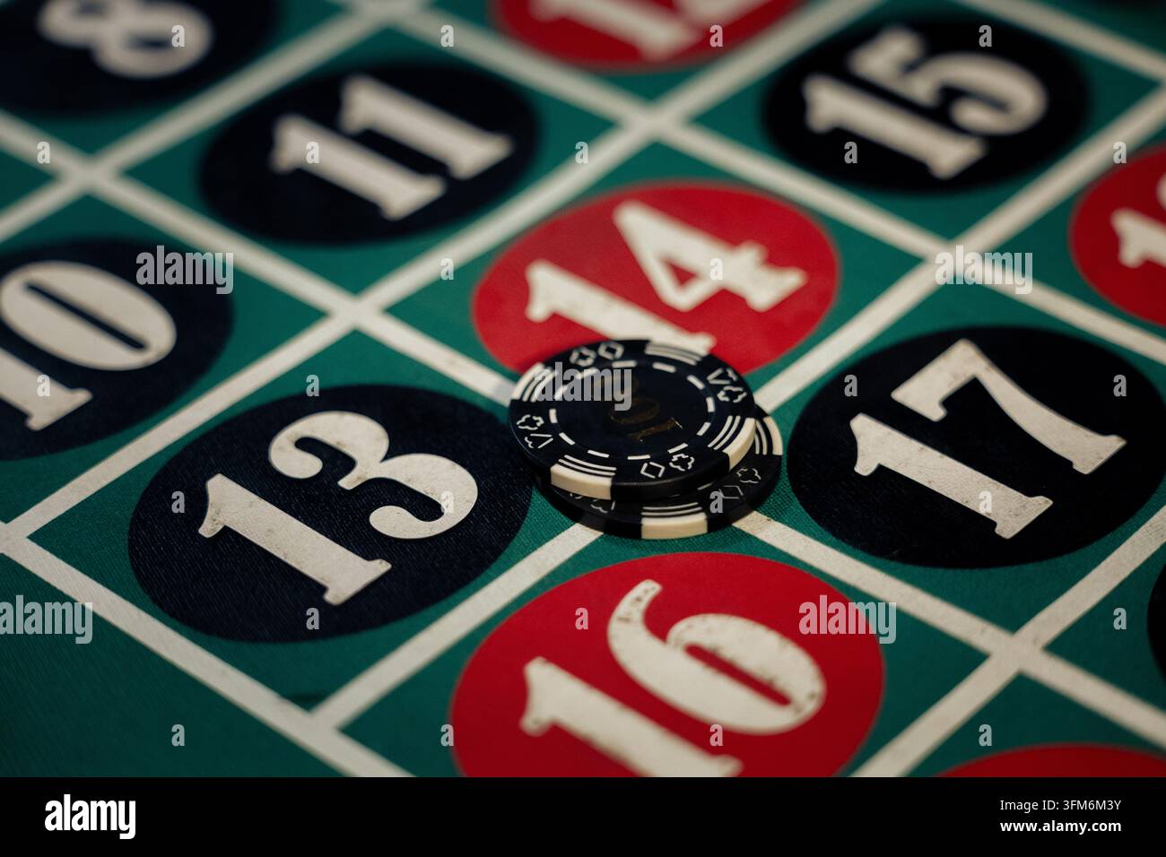 Gettoni da casinò appoggiati su quattro numeri su un tavolo da roulette verde. Gettoni impilati coprono il campo di intersezione sotto una luce intensa. Foto Stock