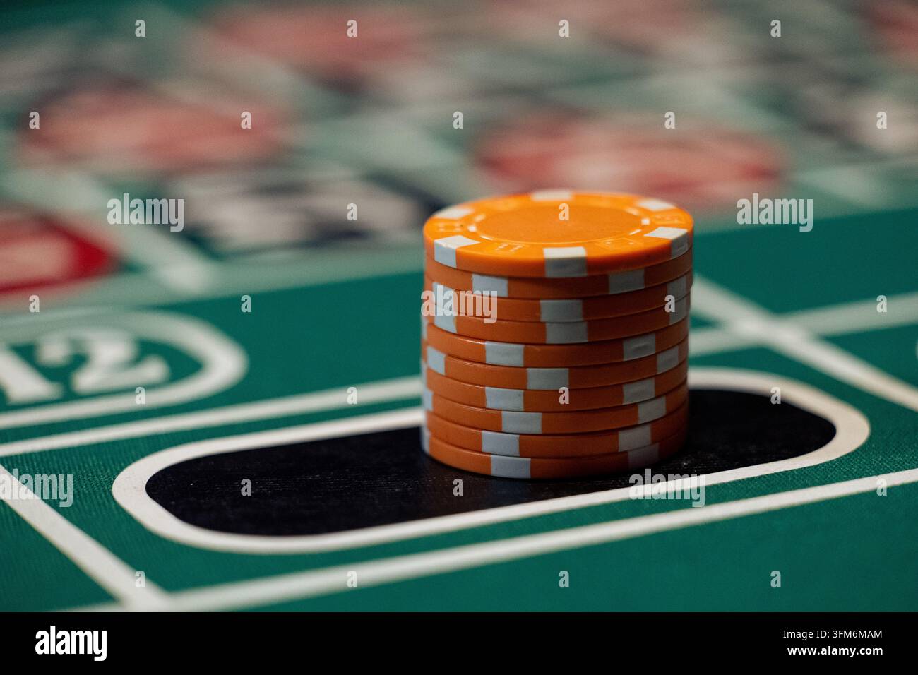 Una pila di gettoni del casinò arancioni posizionati nello spazio di scommessa nero su un tavolo da roulette verde. Primo piano con angolazione bassa. Foto Stock