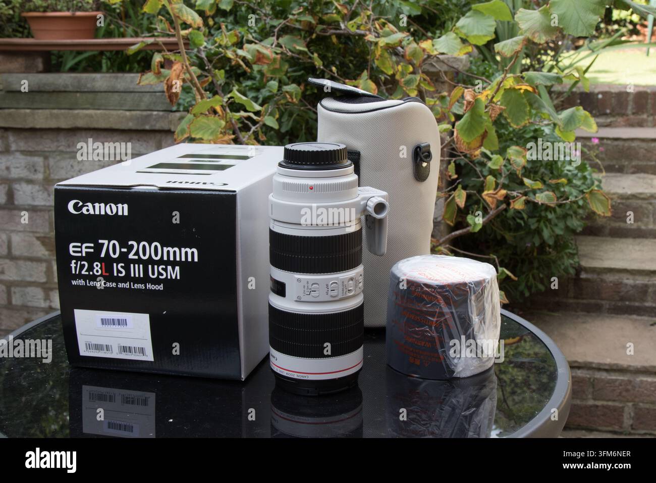 Un teleobiettivo zoom Canon EF 70-200mm f/2.8L IS III USM esposto all'aperto su un tavolo con la sua scatola originale, la custodia morbida e il paraluce. Foto Stock