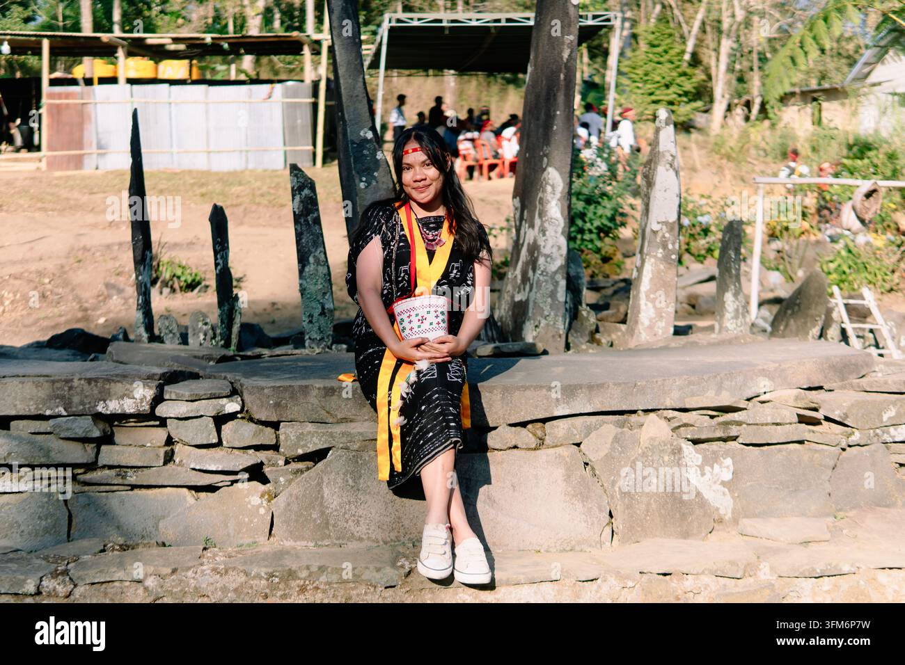Donna indonesiana in abito tradizionale di Bajawa Ngada che posa con i palmi premuti in un sito megalitico, esprimendo ospitalità e patrimonio culturale. Foto Stock
