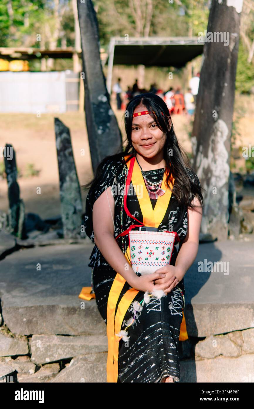 Donna indonesiana in abito tradizionale di Bajawa Ngada che posa con i palmi premuti in un sito megalitico, esprimendo ospitalità e patrimonio culturale. Foto Stock