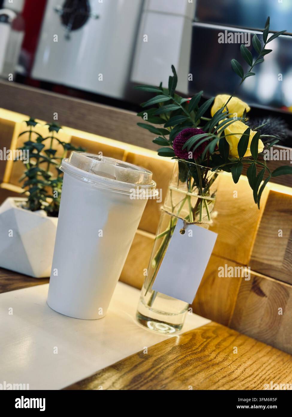 Tazza da caffè da asporto e piccolo vaso di fiori su un tavolo da caffè caldo. - Immagine stock catturata con smartphone