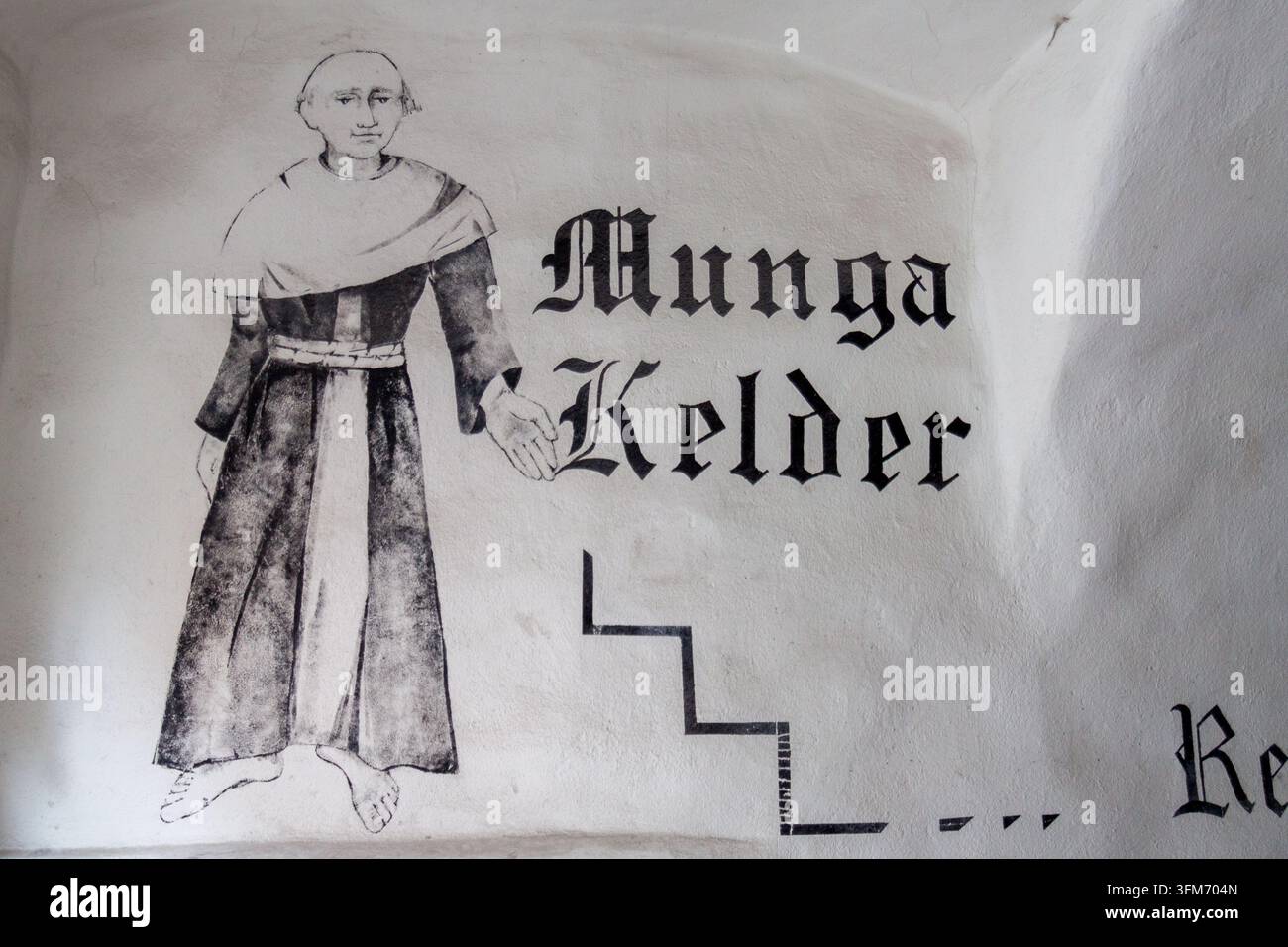 Una figura di monaco dipinta a mano accanto a una scritta in caratteri gotici che legge "Munga Kelder" segna l'ingresso di un ristorante in cantina a Tallinn, in Estonia Foto Stock