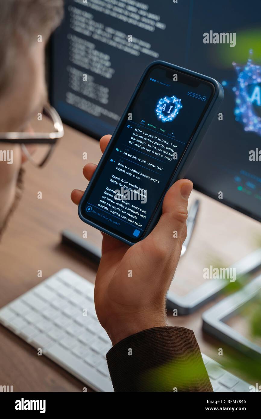 Primo piano di un uomo che utilizza un'app di chatbot AI sul suo smartphone per consigli aziendali, mentre un assistente o agente di intelligenza artificiale sul suo computer lo aiuta con il lavoro e le attività quotidiane sullo sfondo Foto Stock