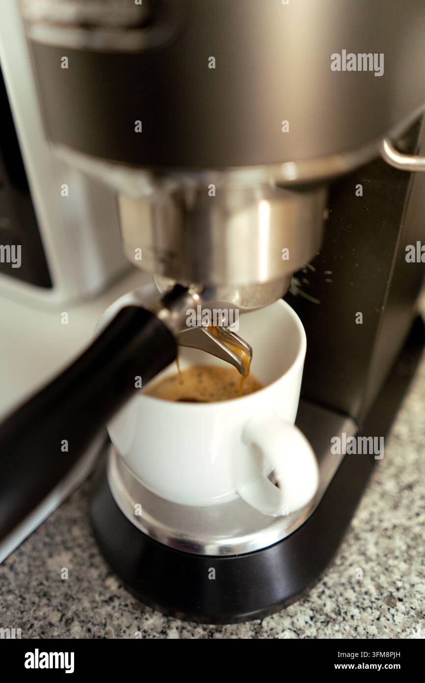 Macchina per l'espresso che versa caffè caldo in una tazza di ceramica bianca su un bancone della cucina Foto Stock