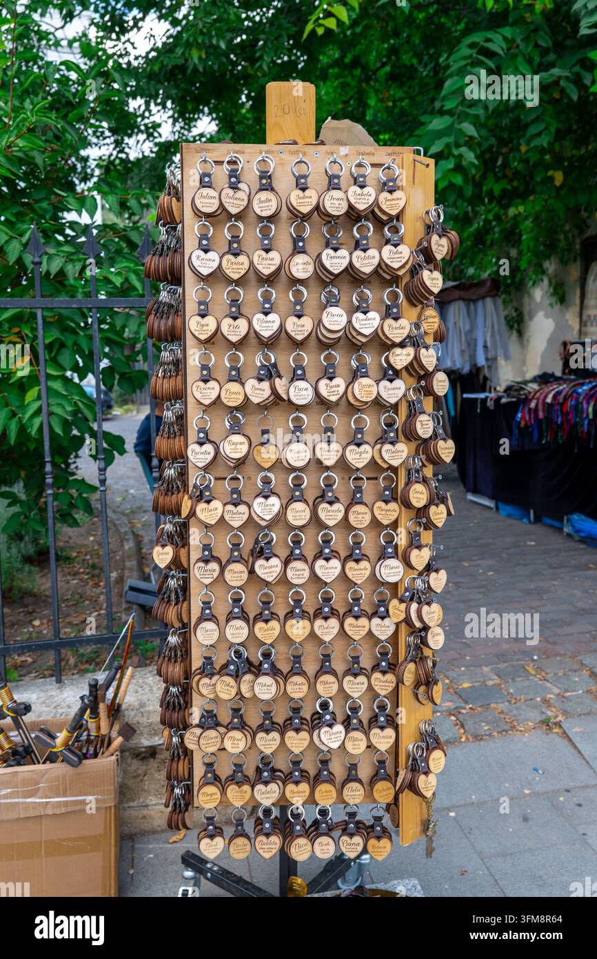 Portachiavi a forma di cuore in legno esposti su un espositore verticale di souvenir in una fiera di strada di mercato turistico all'aperto accanto a una recinzione nera in estate Foto Stock