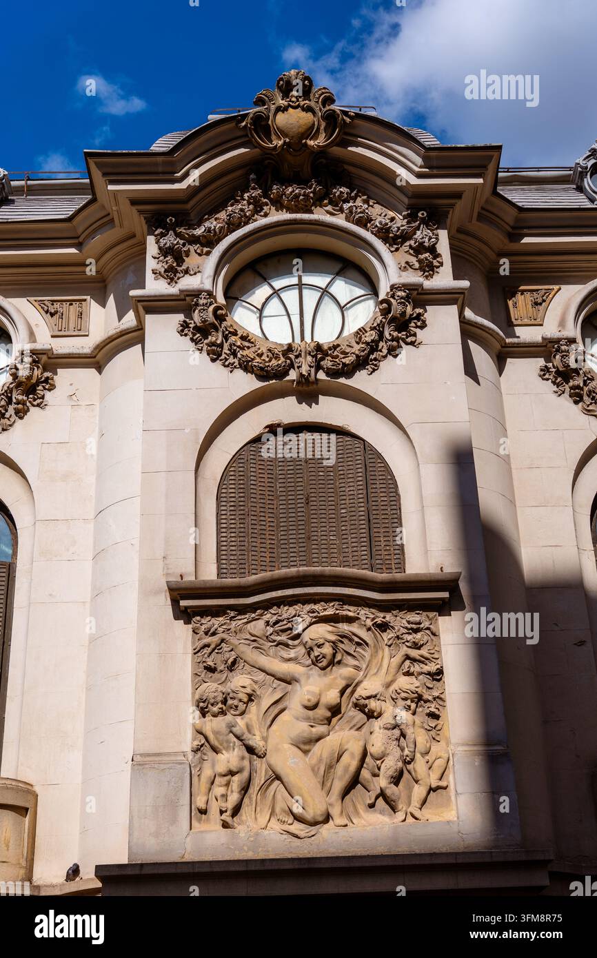 Facciata di edificio storico ornata con un bassorilievo classico in pietra e una finestra rotonda architettonica sotto una scena di cielo blu soleggiato Foto Stock