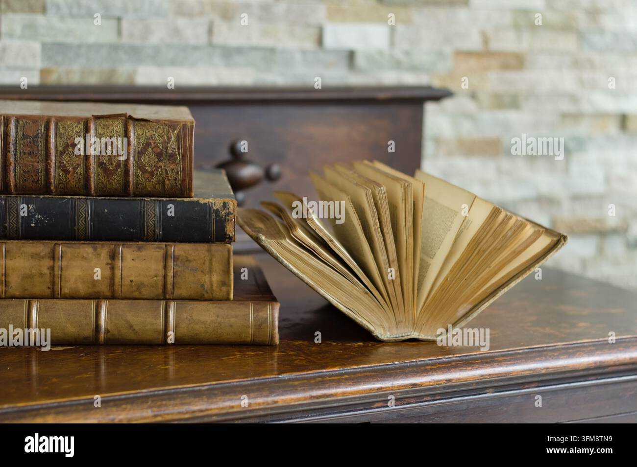 Natura morta di libri rilegati in pelle antichi accanto a un libro vintage aperto con pagine invecchiate, disposti su un tavolo di legno lucido con uno sfondo sfocato Foto Stock