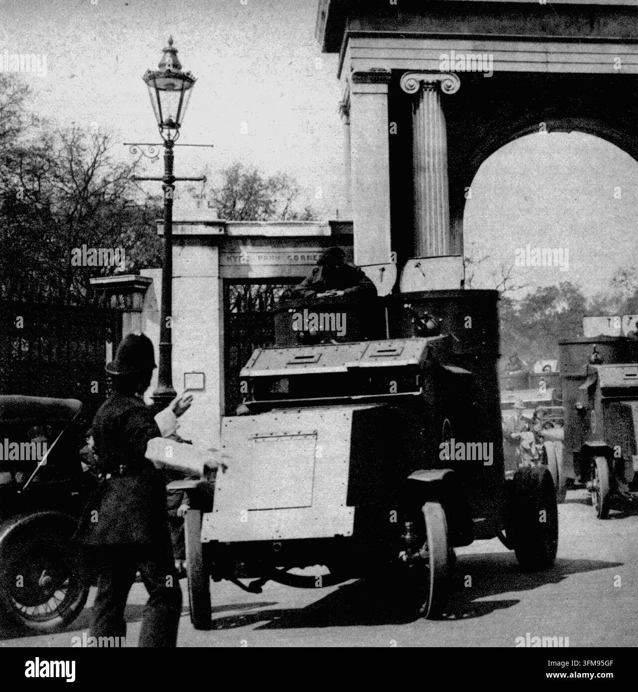 Una fotografia che ritrae un poliziotto in servizio di traffico a Hyde Park Corner, Londra, mentre dirige un'auto blindata dell'esercito britannico attraverso i cancelli. Questo schieramento faceva parte della risposta del governo allo sciopero generale del 1926, durante il quale il personale militare veniva utilizzato per proteggere i servizi essenziali e trasportare rifornimenti di cibo attraverso la città. Il veicolo è un'auto blindata Peerless, un design dell'era della Prima Guerra Mondiale frequentemente impiegato per la sicurezza interna durante gli anni interbellici. 1926. Foto Stock