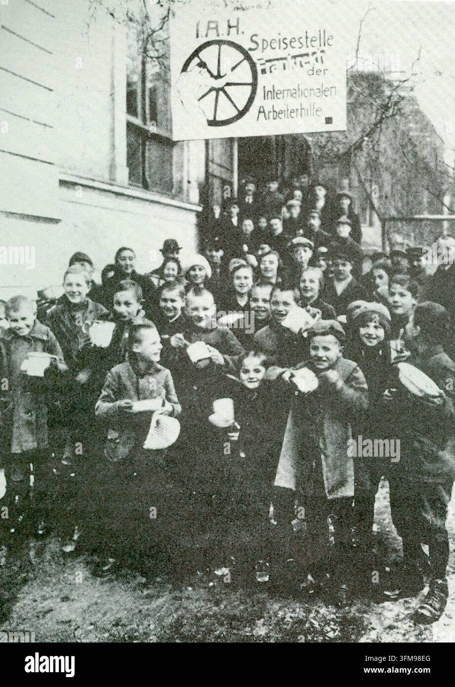 Una fotografia che ritrae bambini tedeschi riuniti fuori da una stazione di alimentazione comunitaria gestita dall'Internationale Arbeit-Hilfe (International Workers' Aid) durante la crisi economica della Repubblica di Weimar. Fondata in risposta alla grave iperinflazione e all'instabilità sociale seguite alla Prima Guerra Mondiale, l'I.A.H. ha fornito un aiuto essenziale attraverso mense popolari e ristoranti comunitari per sostenere le famiglie operaie in difficoltà. Circa il 1923. Foto Stock