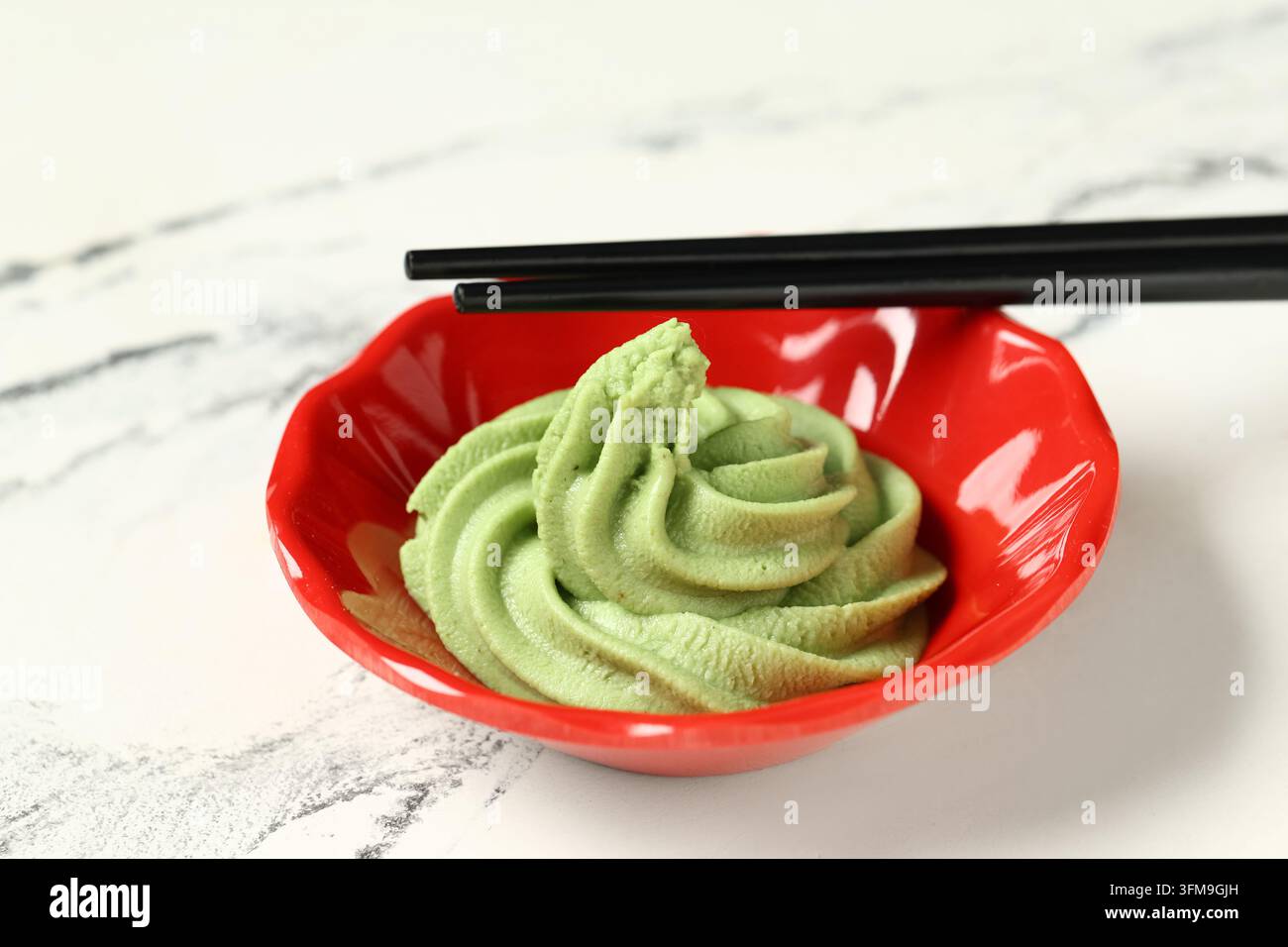 Cucina giapponese e condimento per sushi, pasta di wasabi fresca in una ciotola rossa con bacchette nere per un'esperienza culinaria autentica Foto Stock