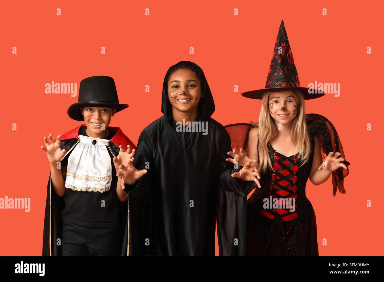 Festa di Halloween e divertimento infantile, gruppo diversificato di bambini in costumi spaventosi che posano con espressioni giocose su uno sfondo studio arancione Foto Stock