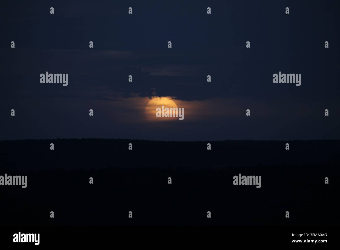 Il sole che tramonta dietro nuvole scure e un orizzonte lontano. Foto Stock
