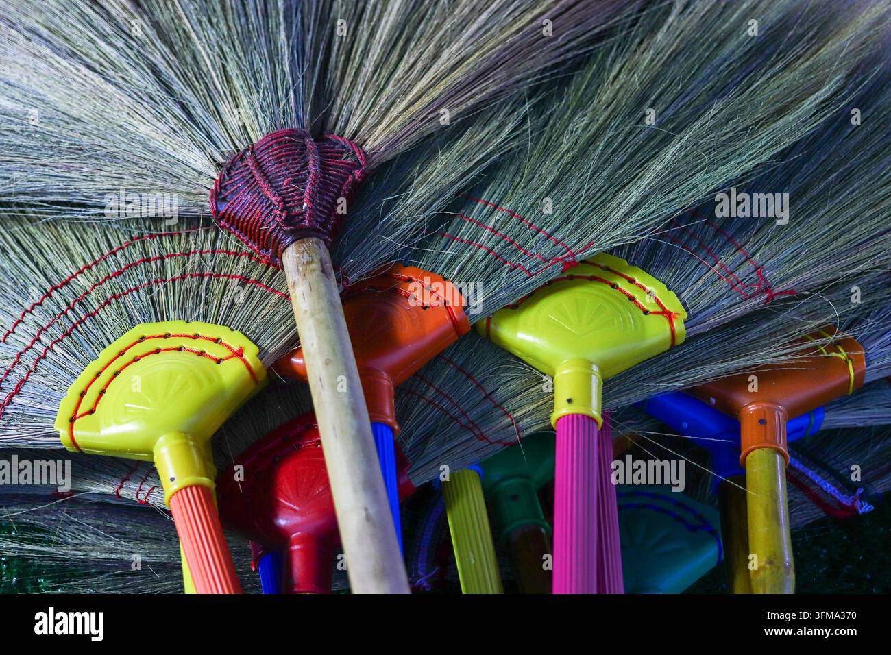 Scopa di paglia con cappucci colorati in plastica e manici di bambù, setole legate con corda rossa, negozio di articoli per la casa, vista dall'alto Foto Stock