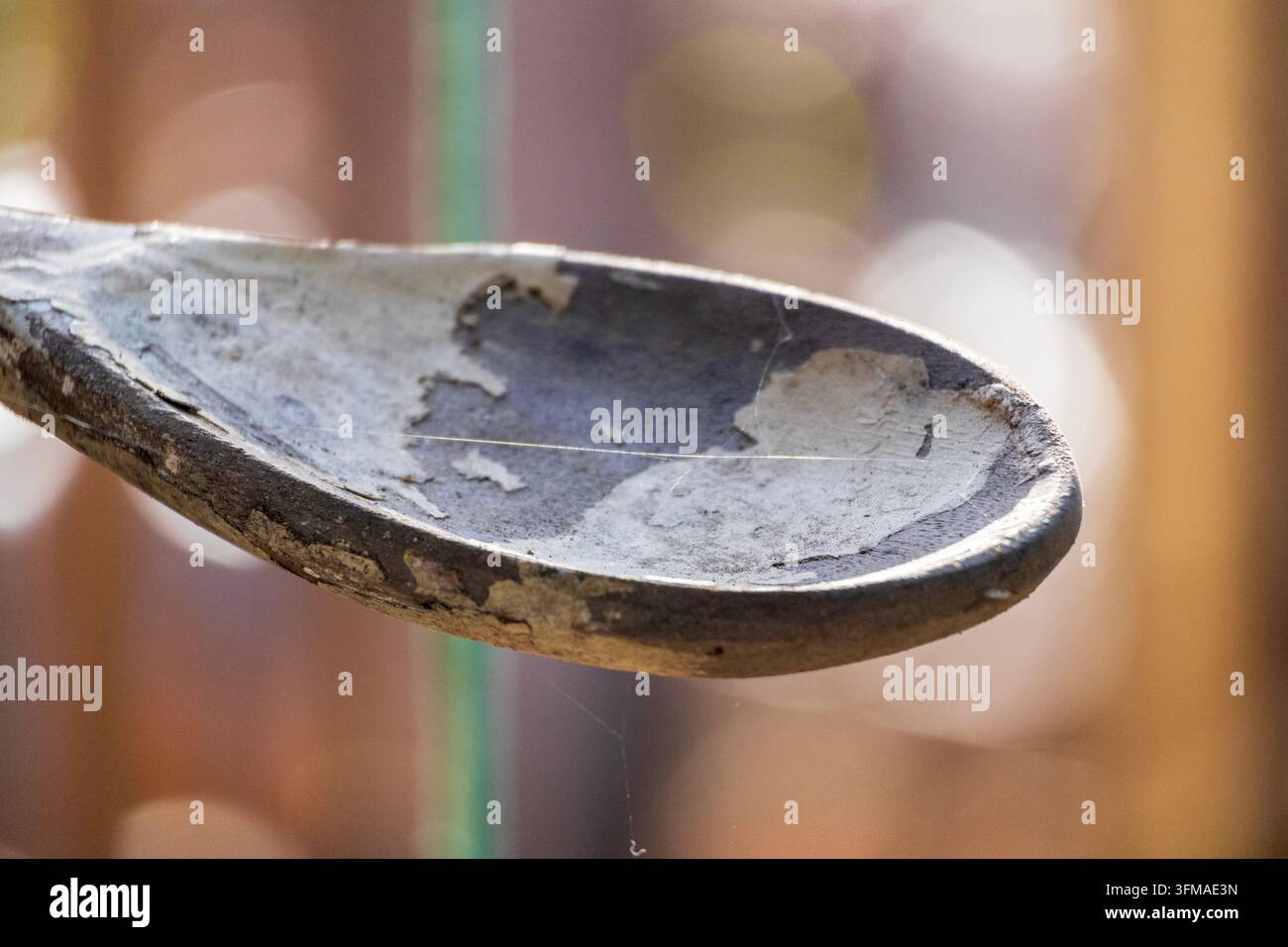 Vista macro dettagliata di un cucchiaio di legno rustico e consumato che mostra superfici logorate e uno sfondo morbido giallo scintillante Foto Stock