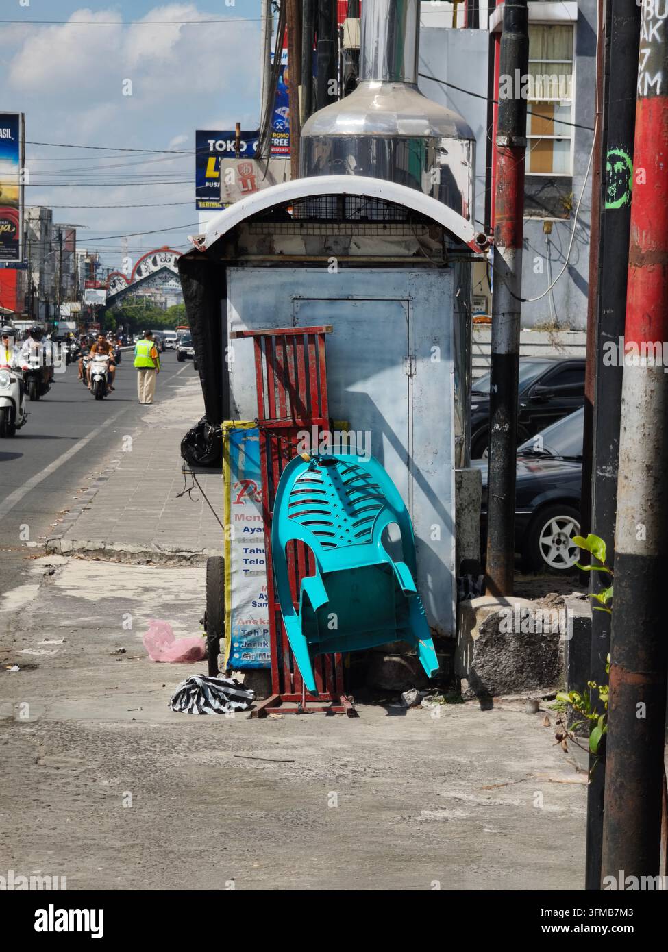 Sedie di plastica colorate impilate accanto a una vecchia fermata dell'autobus su una strada trafficata in un'area urbana sotto un cielo blu terso Foto Stock