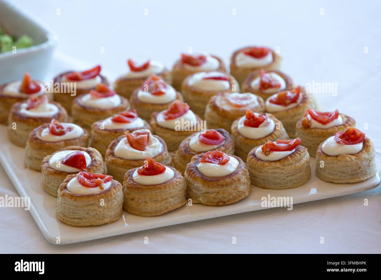 Pasticcini mini vol-au-vent ripieni di formaggio fresco saporito e con guarnizione di pomodorini freschi Foto Stock