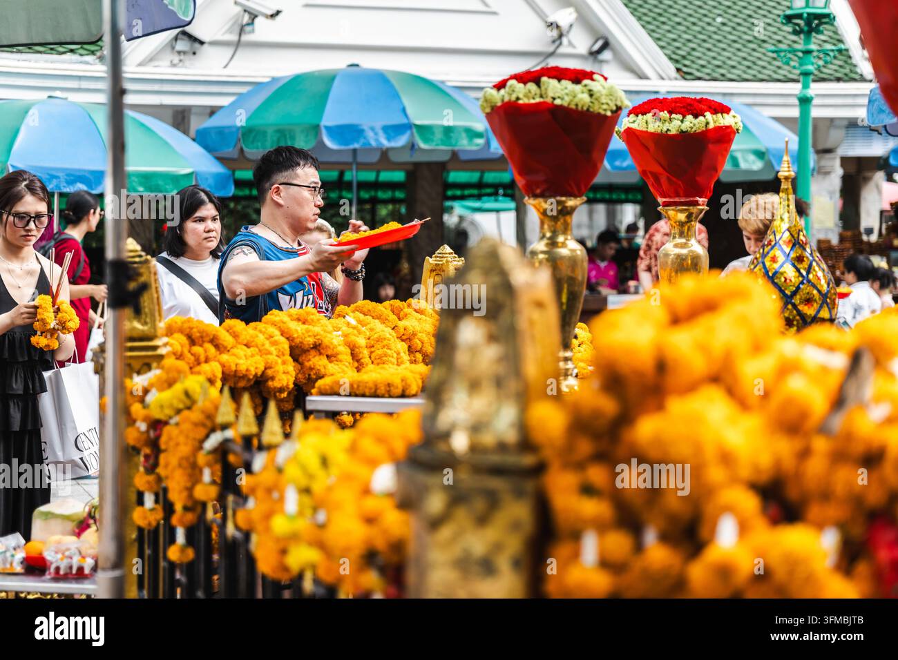 Bangkok, Thailandia, 4 maggio 2026: Visitatori che osservano offerte di fiori di campo luminosi e esposizioni floreali in un mercato di Bangkok, con oggetti decorativi buddisti Foto Stock