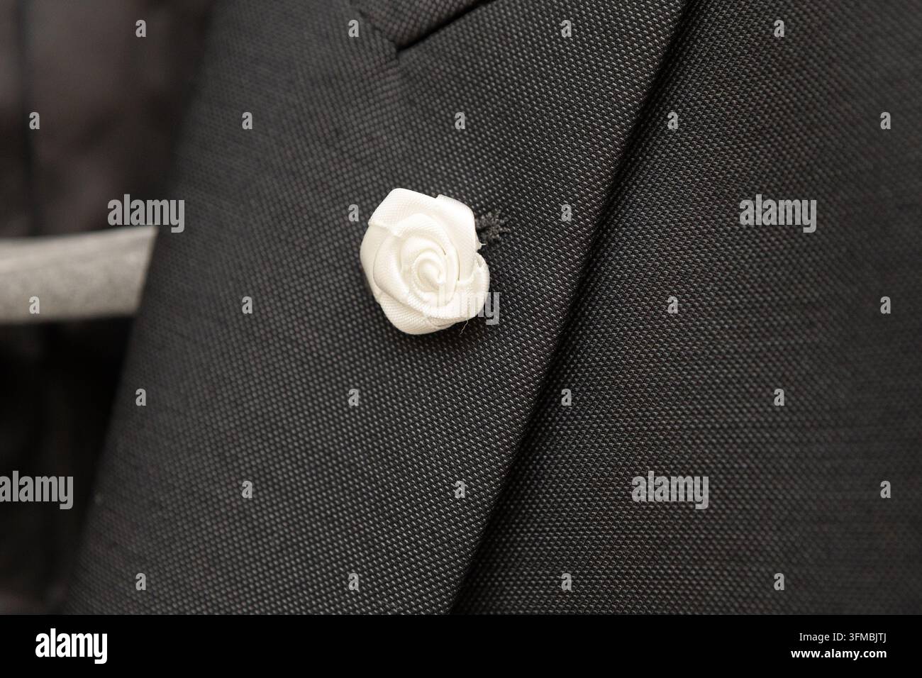 Spilla a forma di rosa in tessuto bianco che adorna una giacca da completo formale nera Foto Stock