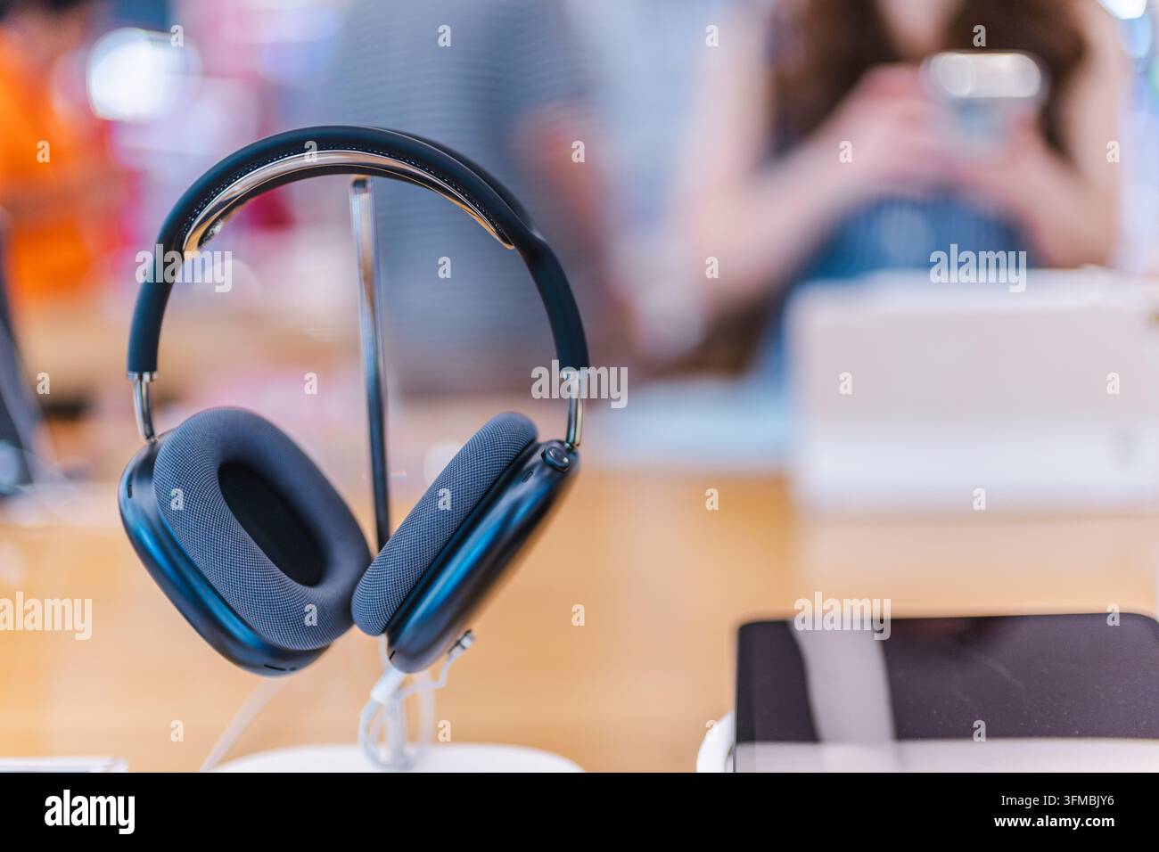 Bangkok, Thailandia, 4 maggio 2026: cuffie over-ear Apple AirPods Max 2 appoggiate su un espositore da tavolo, con una persona e un laptop sfocati sullo sfondo. Foto Stock