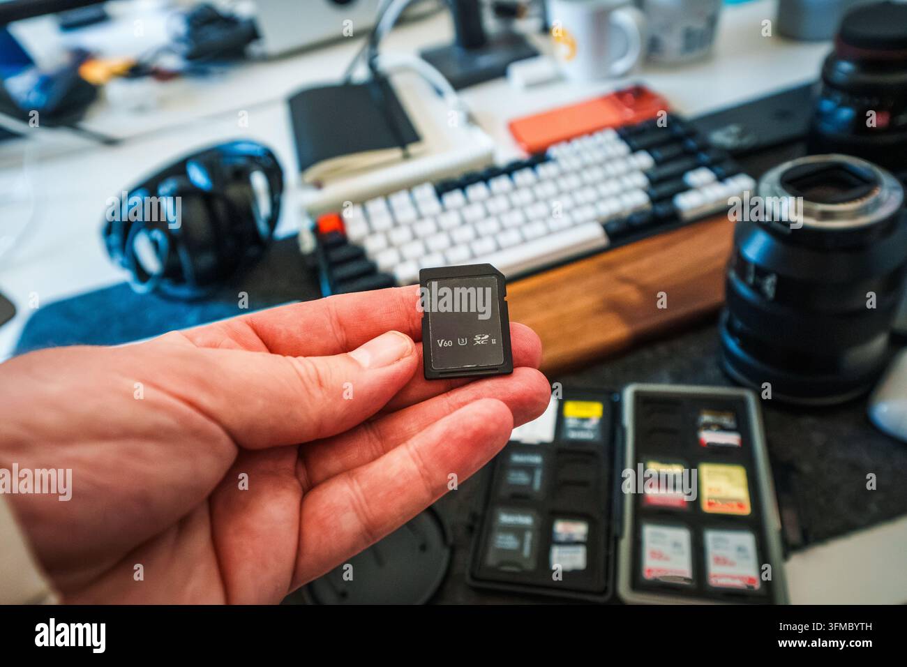 Lettore di schede di memoria capacità di archiviazione backup trasferimento file scrivania. Una mano tiene una scheda memoria SD ad alta velocità sopra una custodia organizzativa ripiena di vari di Foto Stock