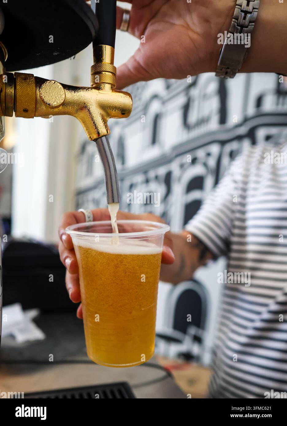 Un barista versa una birra fresca alla spina da un rubinetto d'oro lucente in un bicchiere di plastica. Foto Stock
