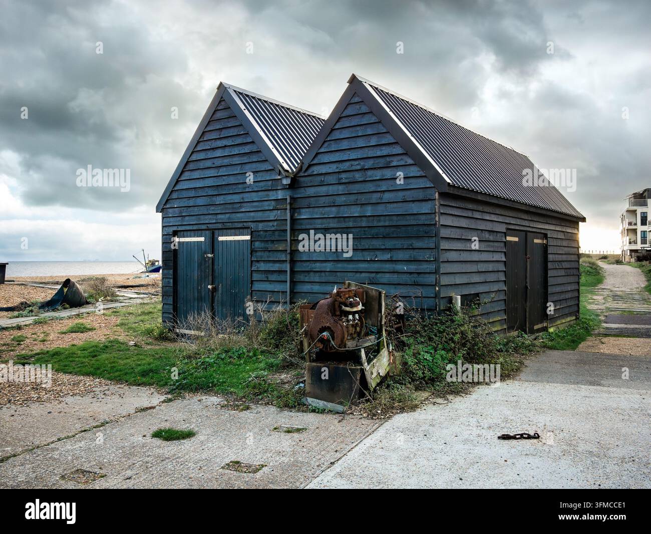 Un capanno di stoccaggio per pescatori si trova su Hythe Beach nel Kent, sotto un cielo cupo e nuvoloso Foto Stock