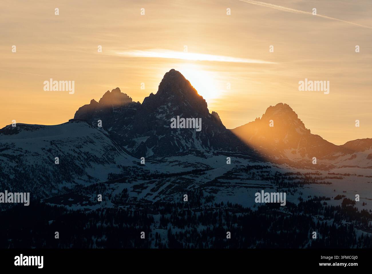 Il sole splende dietro imponenti vette montuose coperte di neve. Foto Stock