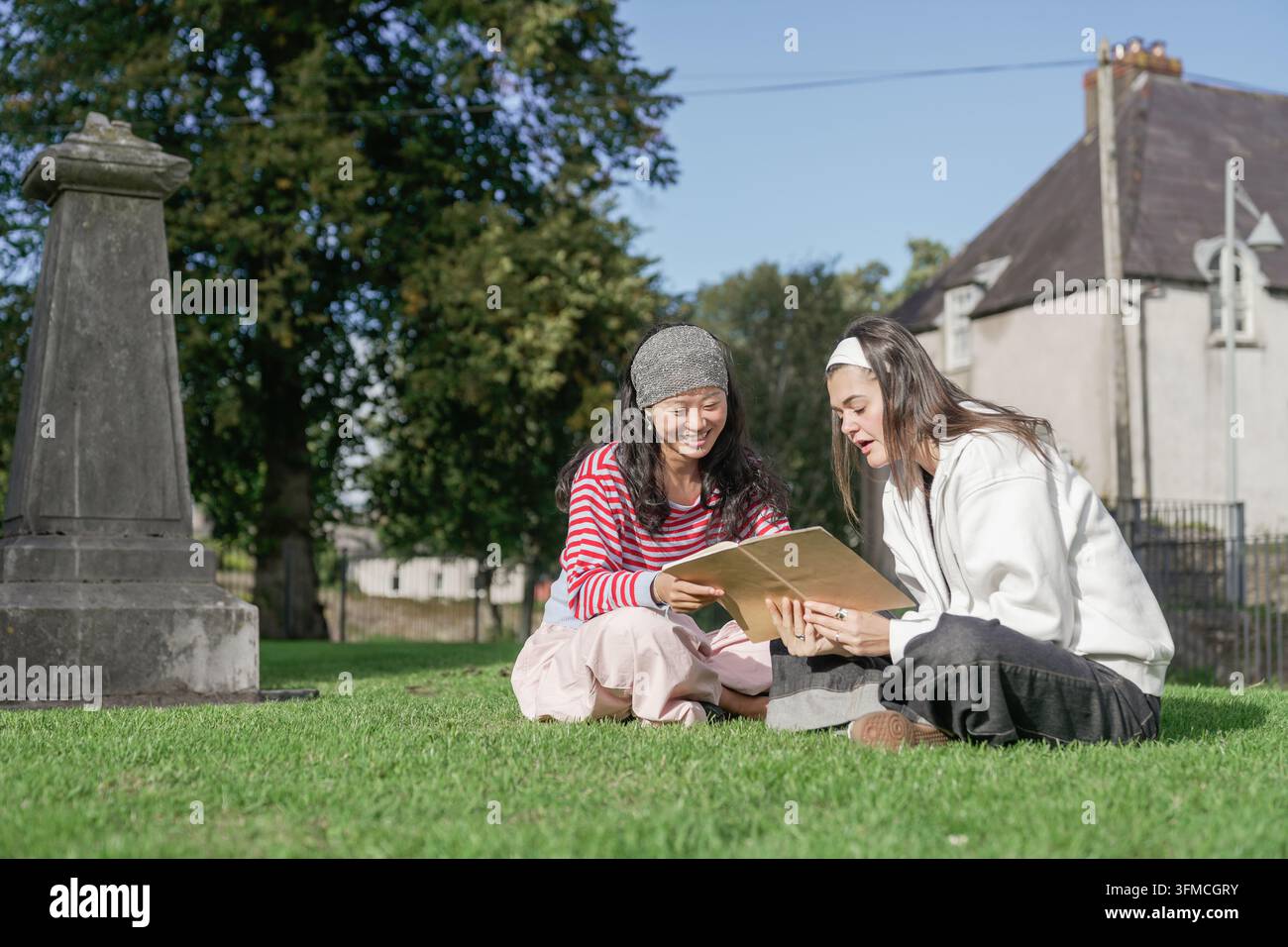 Giovani donne che studiano insieme un libro in un cimitero Foto Stock