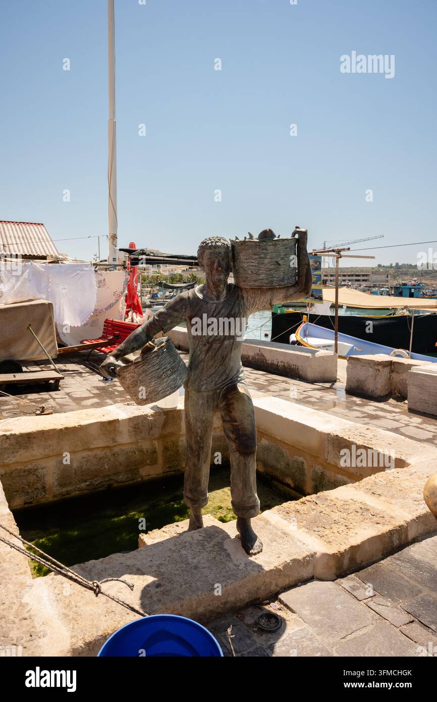 Statua di bronzo di un pescatore su un molo soleggiato del porto a Malta Foto Stock
