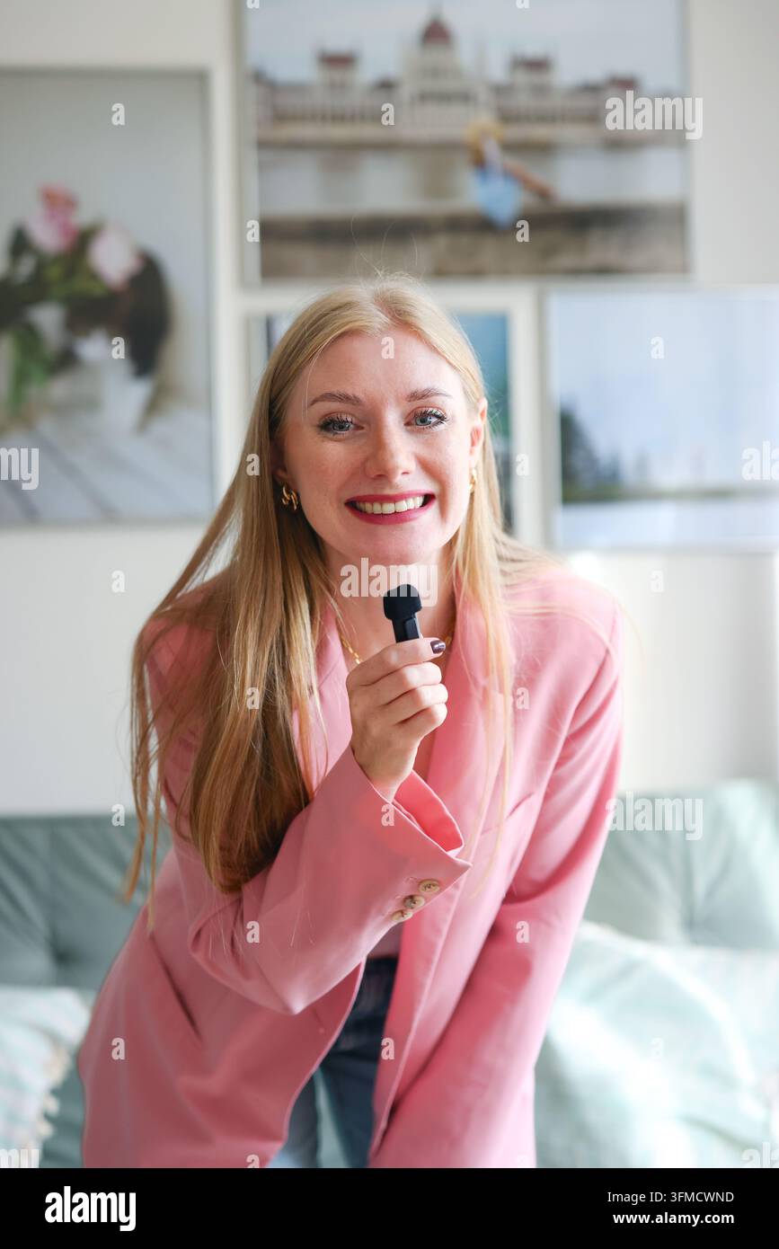 Presentatrice sorridente parla in un microfono a casa, ideale per podcasting, educazione online, branding personale e contenuti multimediali. Foto Stock