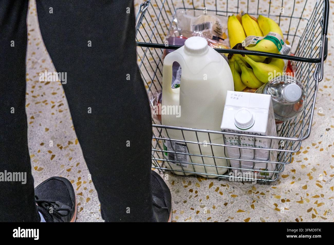 Londra, Regno Unito, 28 settembre 2026, Primo piano di un cestino della spesa pieno di latte fresco, una confezione di latte a lunga conservazione e banane Foto Stock