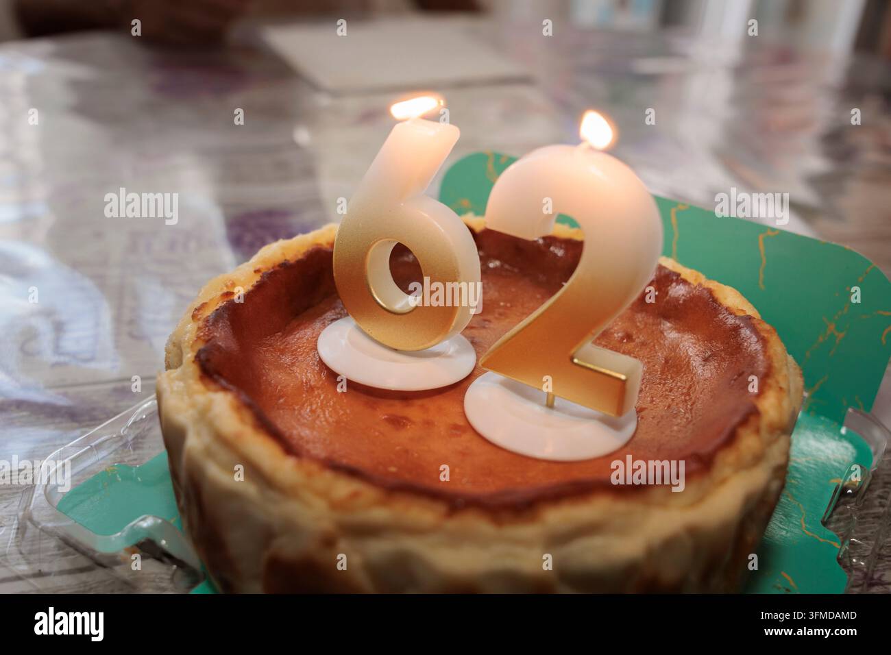 Cheesecake di compleanno con candele accese che mostrano il numero 62 Foto Stock