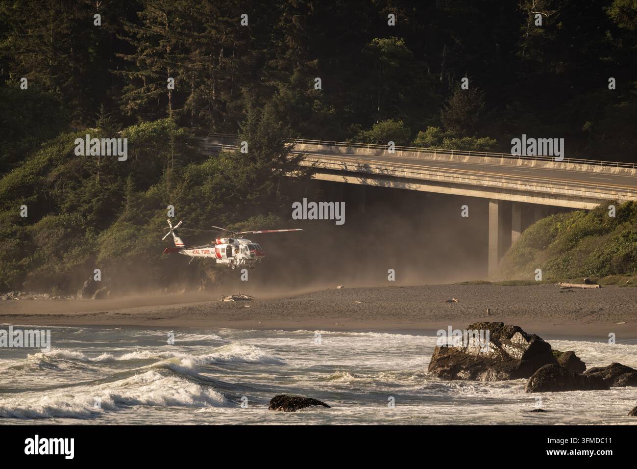Crescent City, Stati Uniti: 10 luglio 2025: Elicottero decolla dalla spiaggia sotto un ponte lungo la costa di Redwood Foto Stock