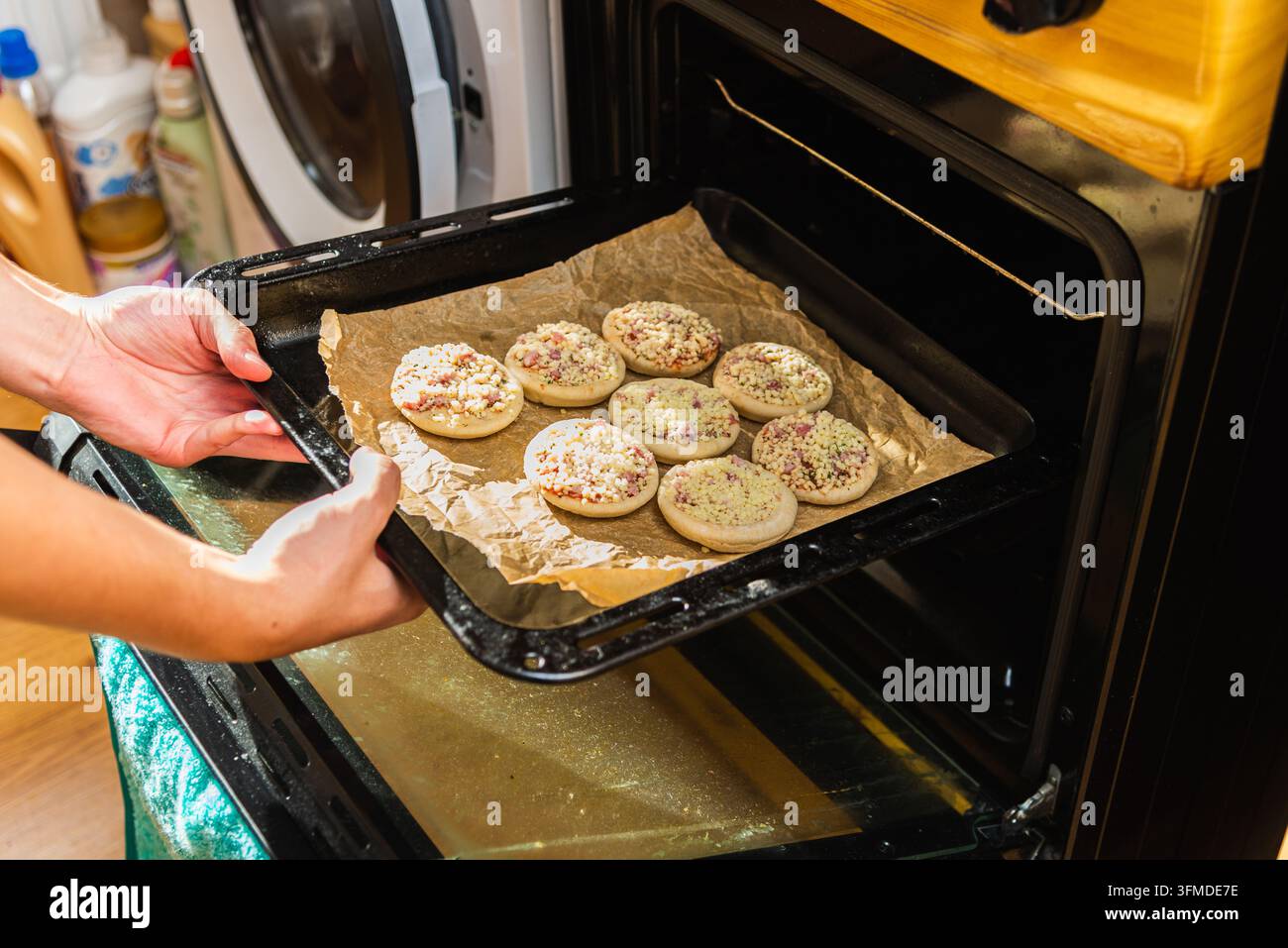 Persona che tiene una teglia con mini pizze surgelate non cotte dirette verso il forno. Foto Stock